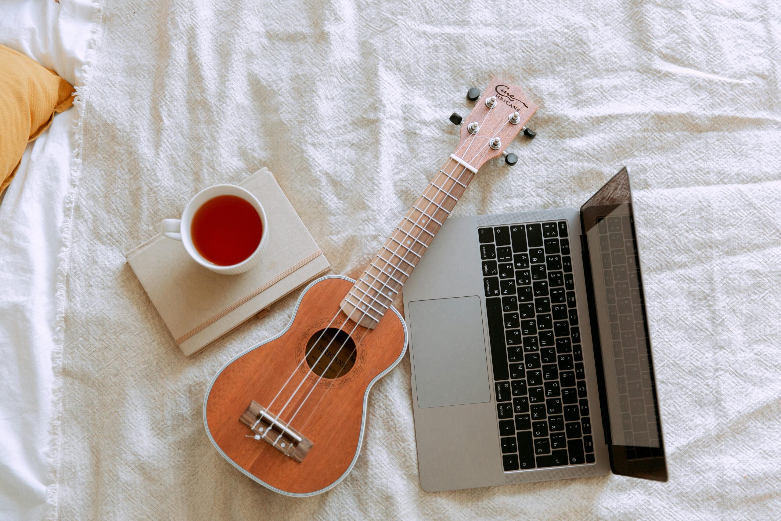 A cozy composition featuring a ukulele, laptop, and cup of tea on a bed for a relaxing indoor ambiance.